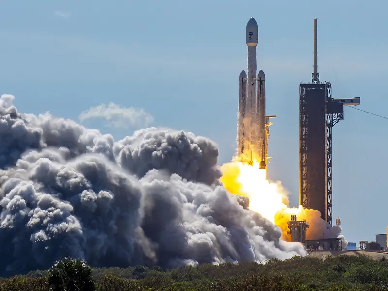 A big rocket lifting off on bright flames against a blue sky