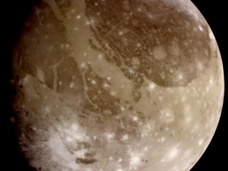 A large grey and brown moon with bright patches and darker regions
